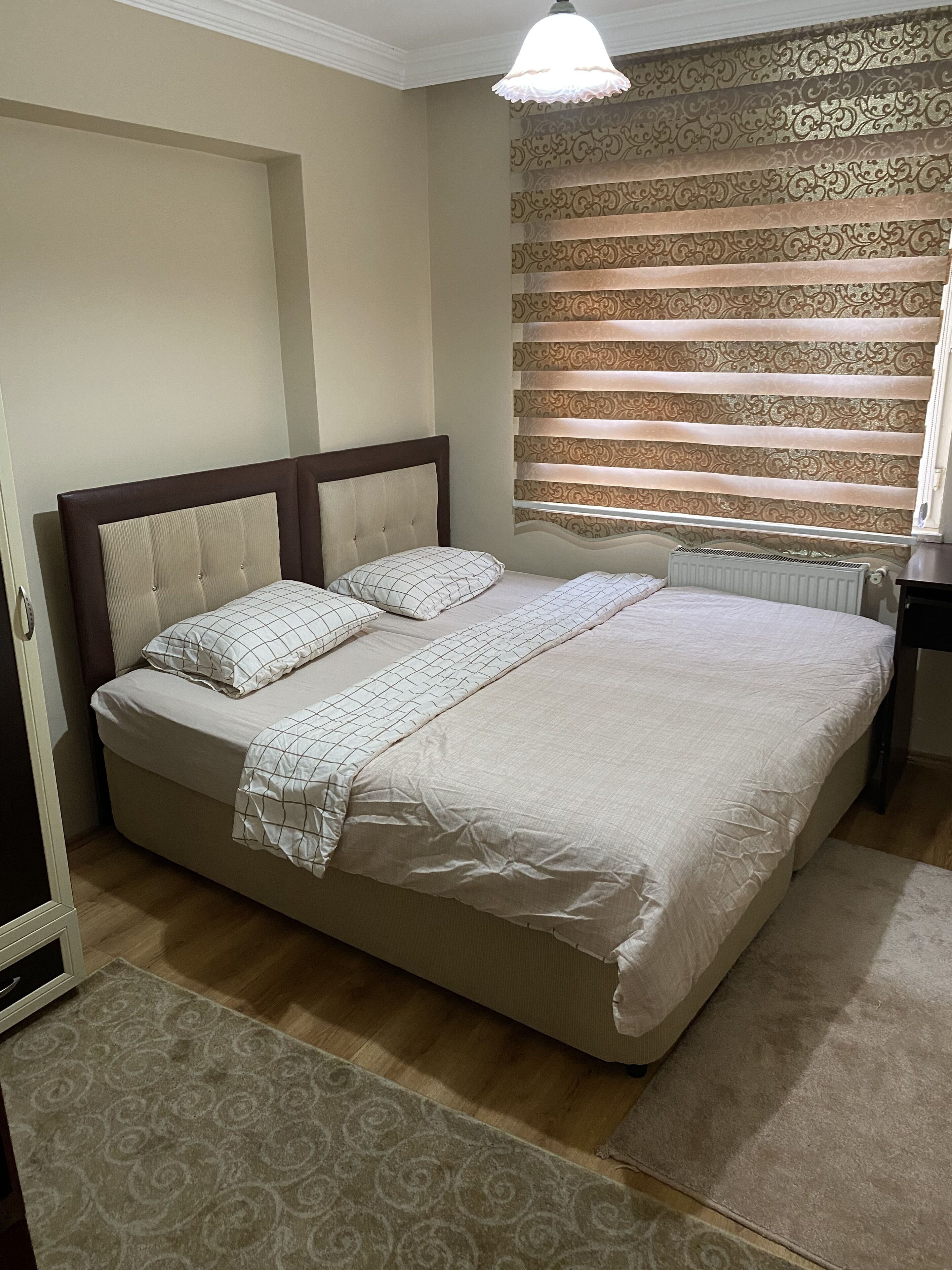 A bedroom with a large bed, a radiator, patterned curtains, and a ceiling light.