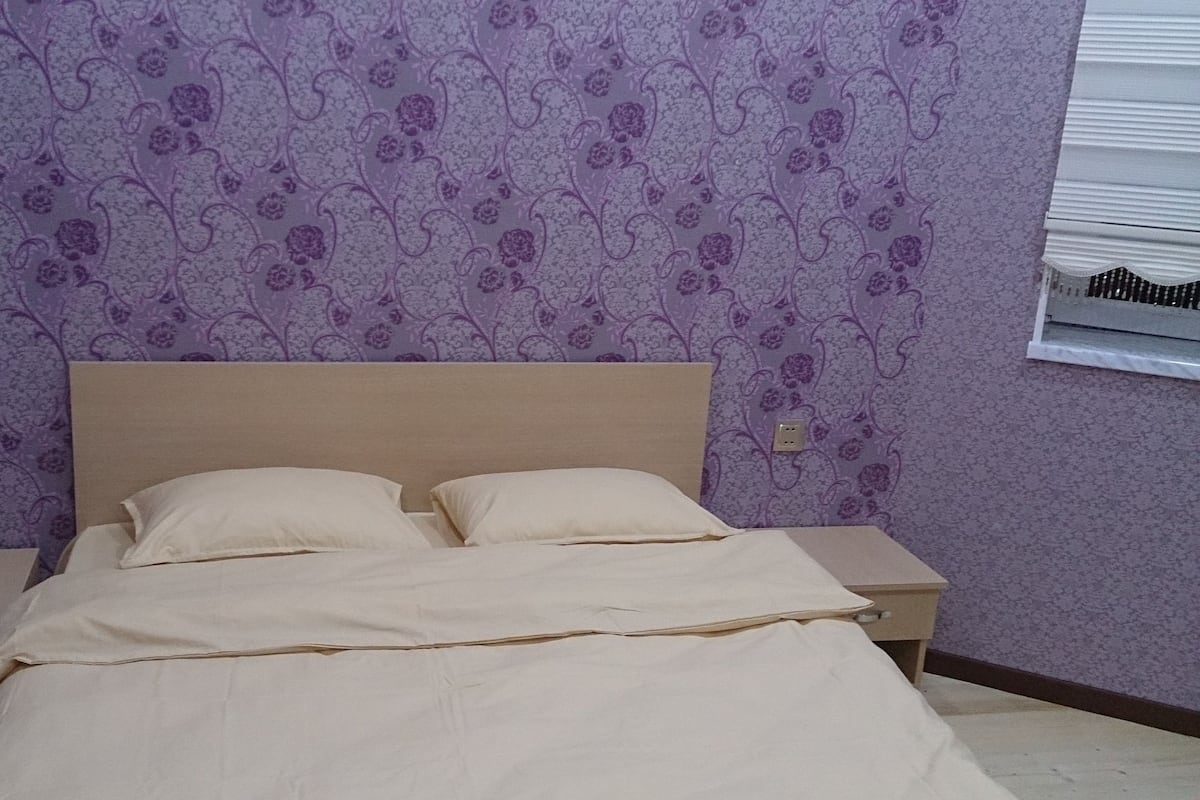 A bed with two pillows, a wooden headboard, and a nightstand with a lamp.