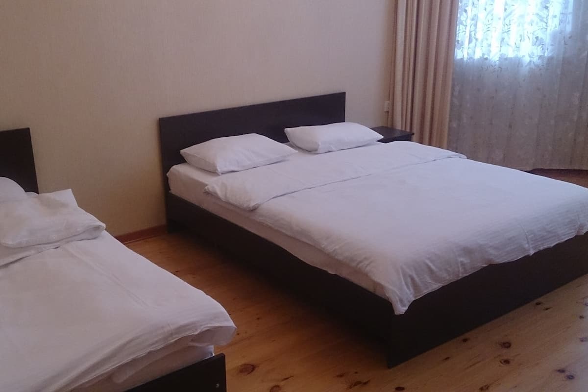A room with two single beds, each with white bedding and a dark headboard. The room has wooden flooring and a plain wall.