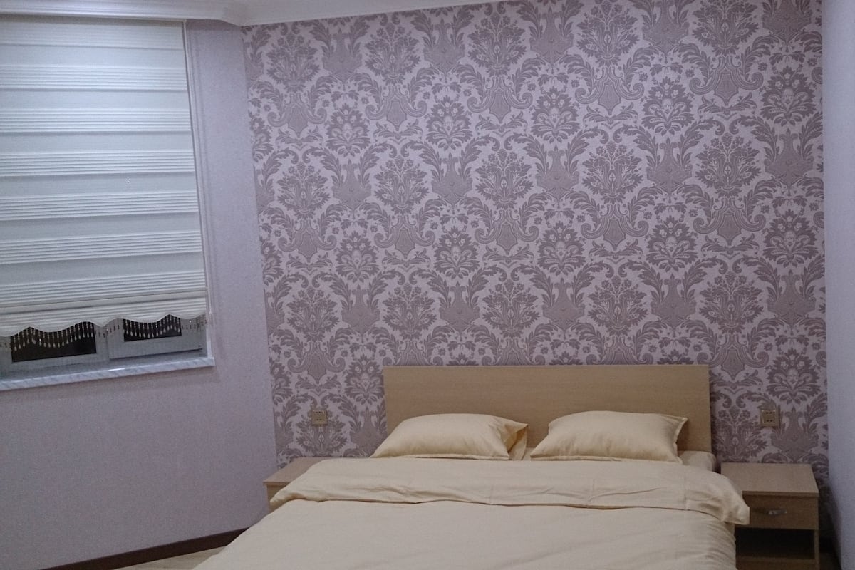 A bedroom with a bed, nightstands, and a window with blinds.