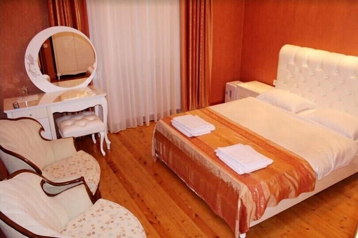 A hotel room with a bed, a vanity with a mirror, two chairs, and a window with curtains.
