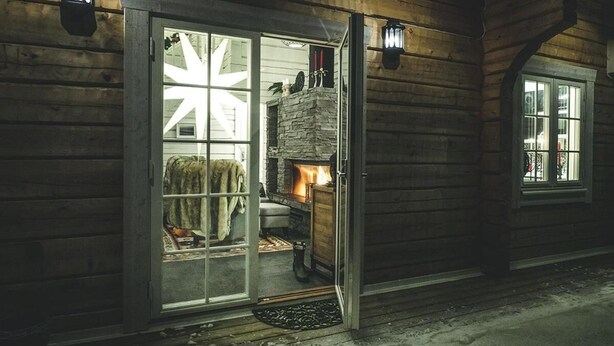 A wooden building with a glass door leading to a room with a fireplace. - Sara's Bed and Breakfast (Erikslund)