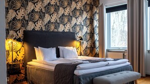 A neatly made bed with a dark headboard, a bedside table with a lamp, and a window with curtains. - Hensbacka Hotell (Munkedal)