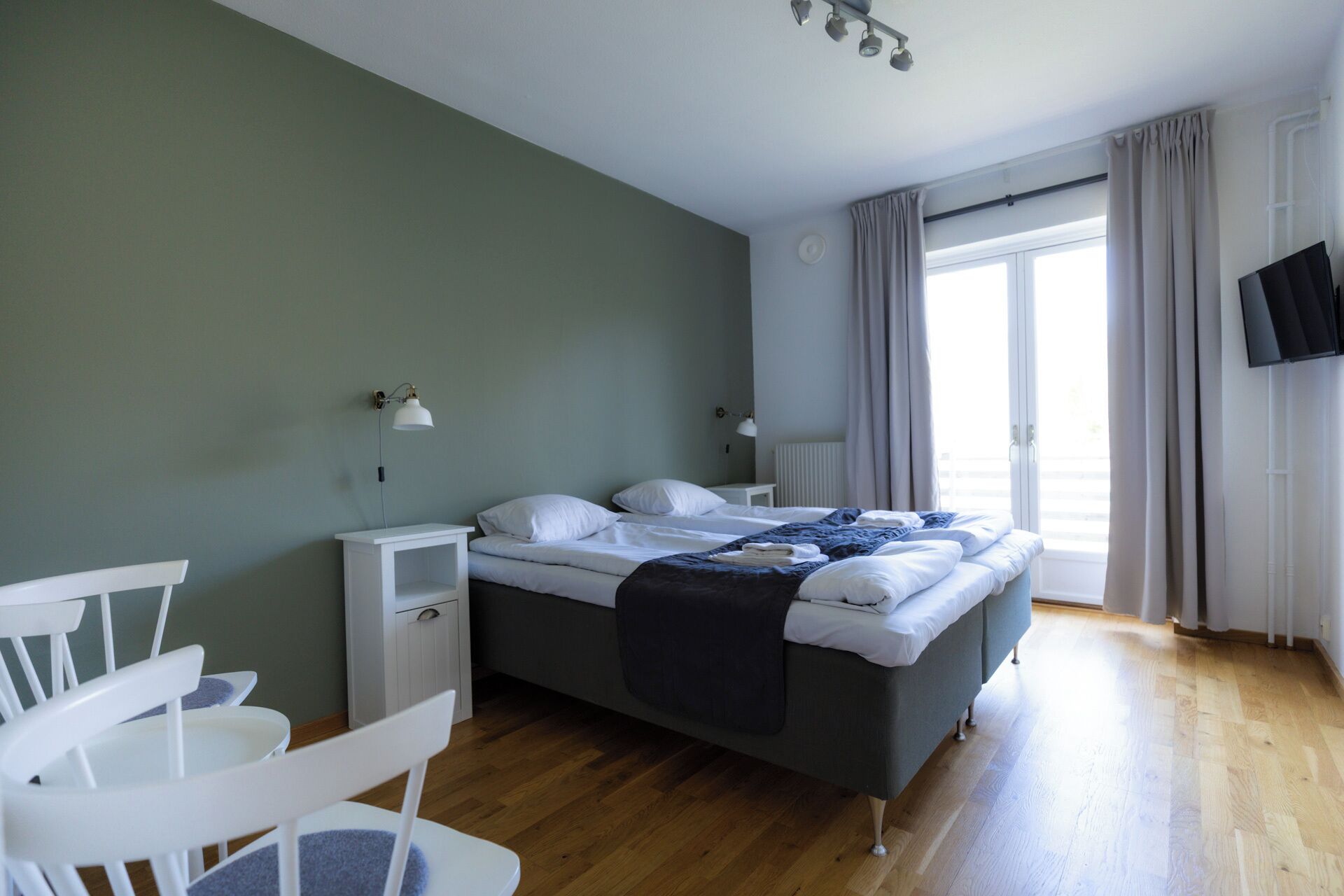 Quarto com cama, mesas de cabeceira, uma cadeira, televisão e janela com cortinas.