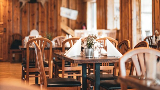 A restaurant interior with wooden walls, ceiling beams, and tables set for dining. - Hensbacka Hotell (Munkedal)