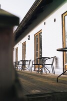 A row of outdoor tables and chairs with a white brick wall and large windows in the background.