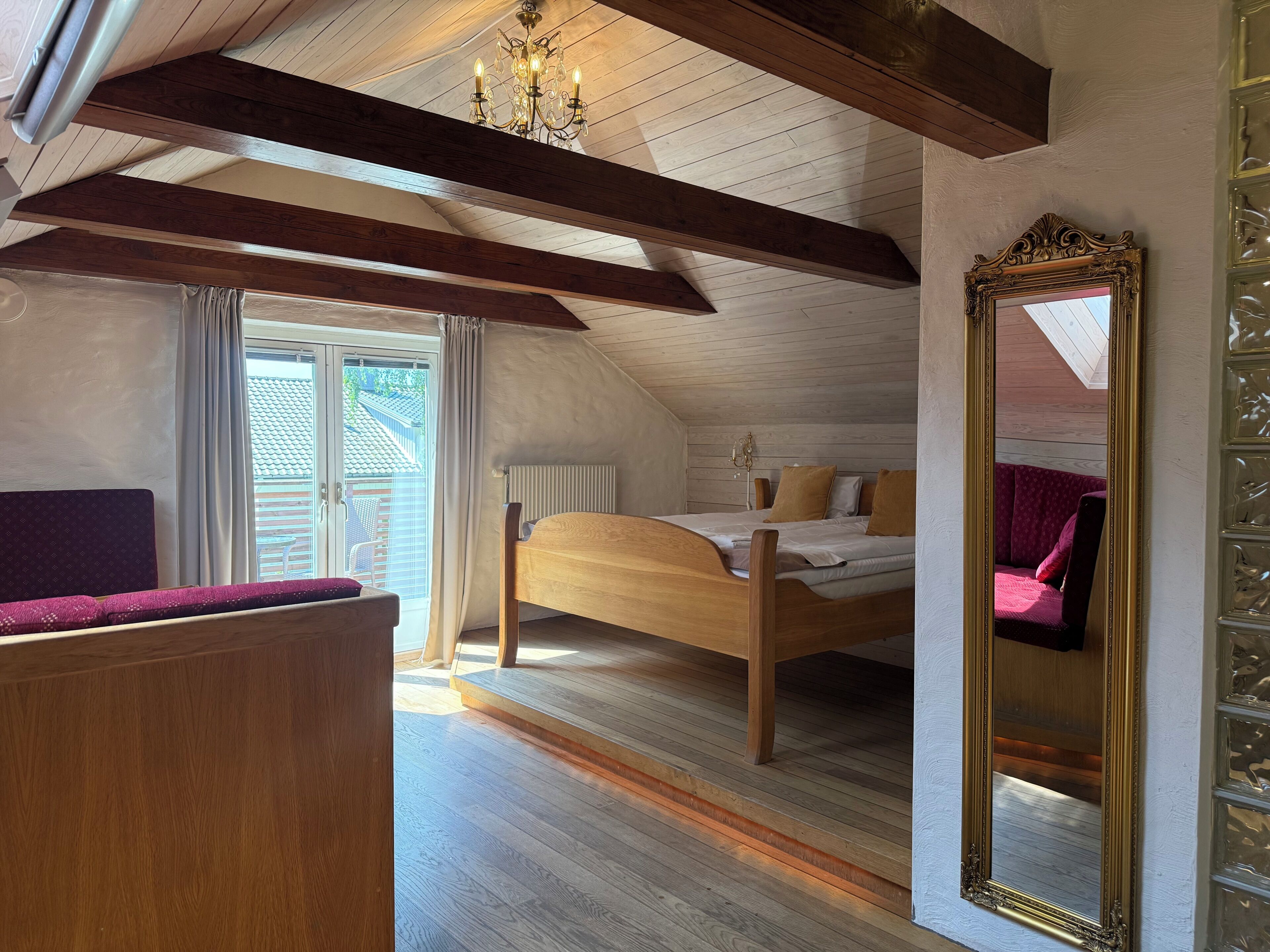 A bedroom with a wooden bed, a large mirror, and a window with curtains.