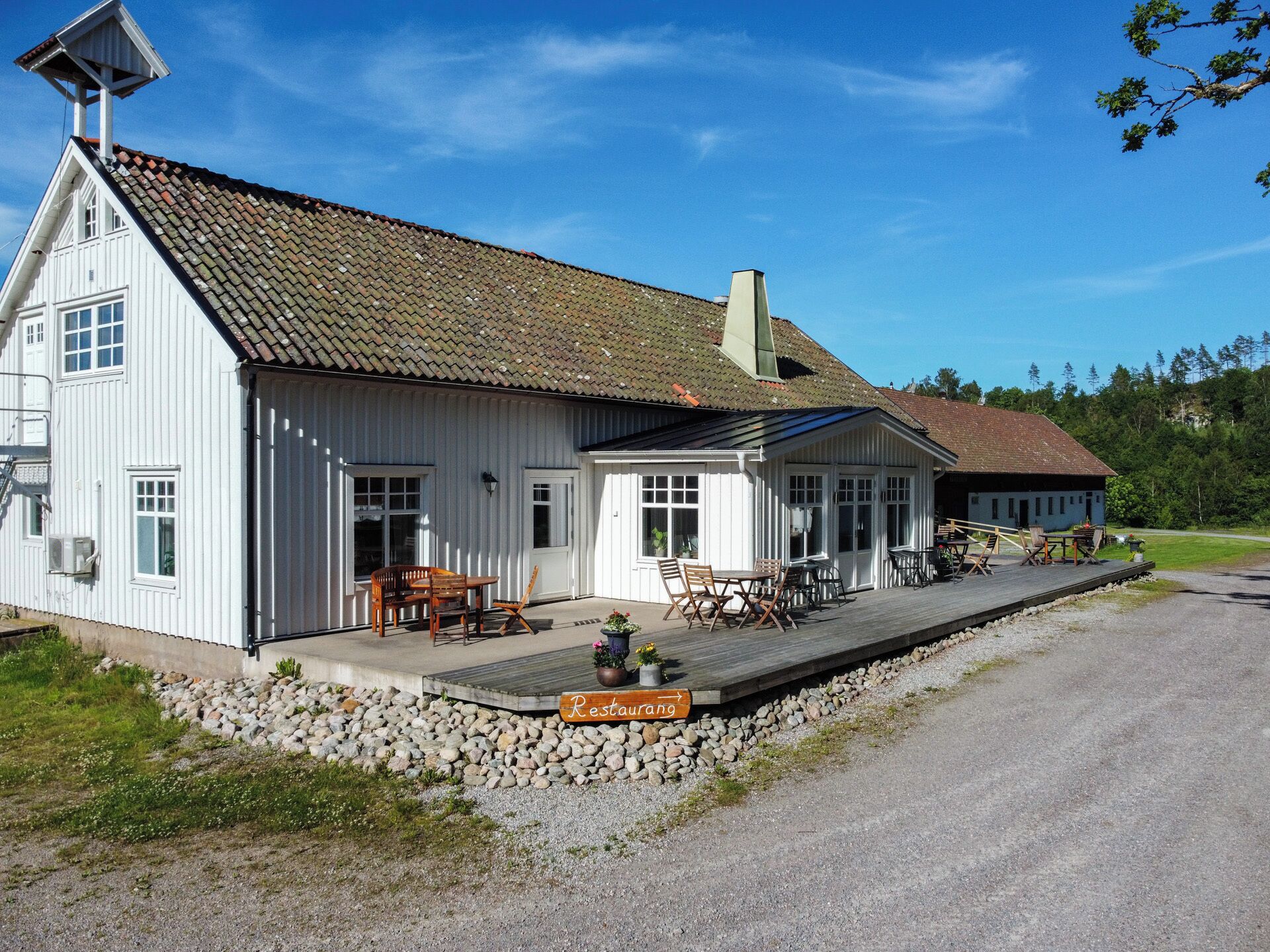 A white building with a sloped roof, a porch with outdoor seating, and a sign indicating a restaurant.