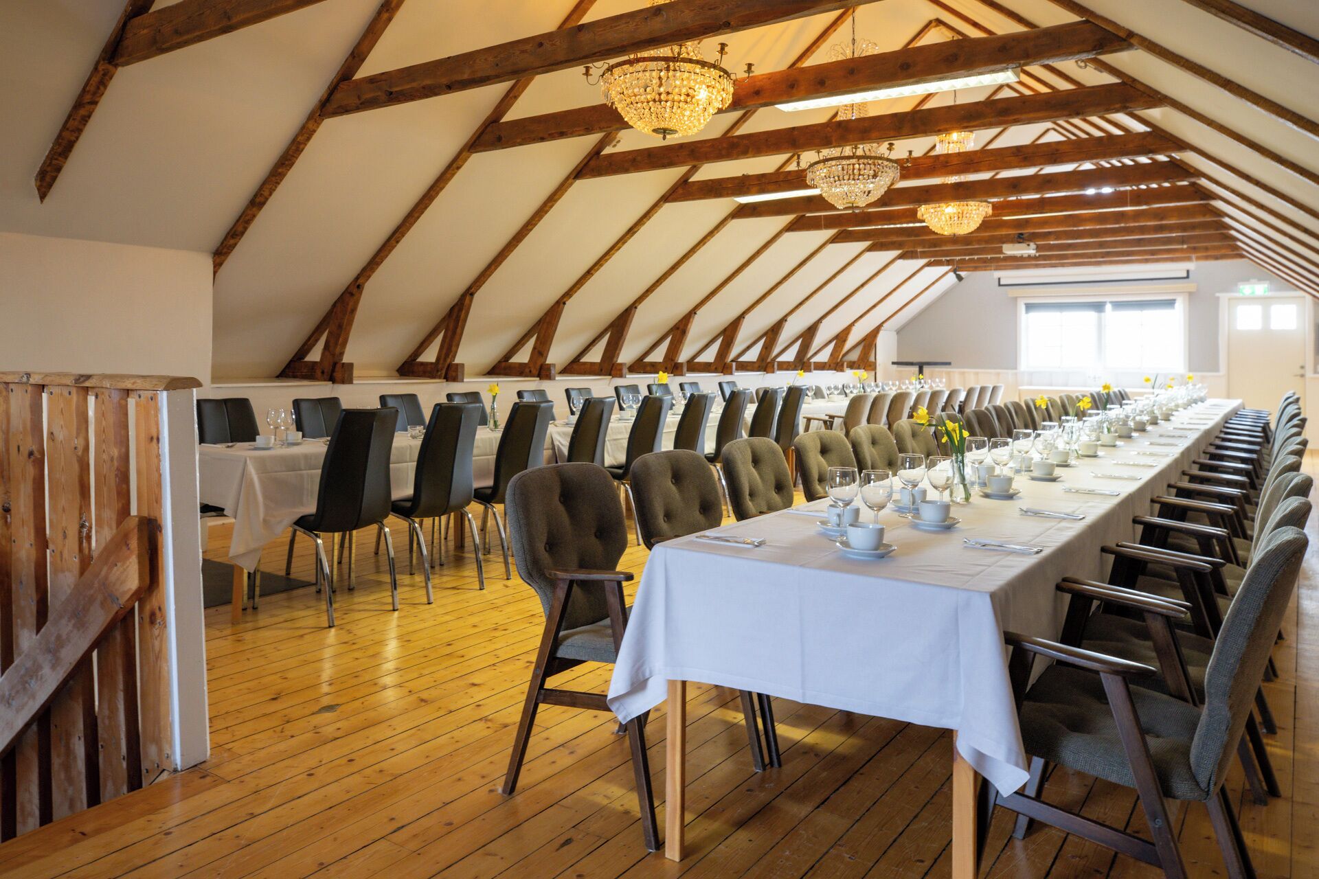 Une longue table à manger entourée de chaises, des poutres en bois et des lustres dans une pièce spacieuse.