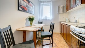 Uma cozinha com armários de madeira, fogão, mesa de jantar com cadeiras e janela com cortinas leves.