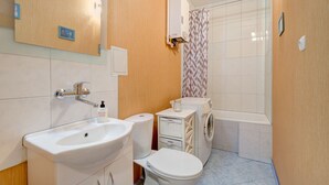 Casa de banho com lavatório, sanita e máquina de lavar roupa.