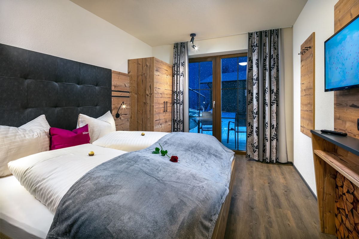 A modern hotel room with a large bed, a TV, and a balcony with curtains.