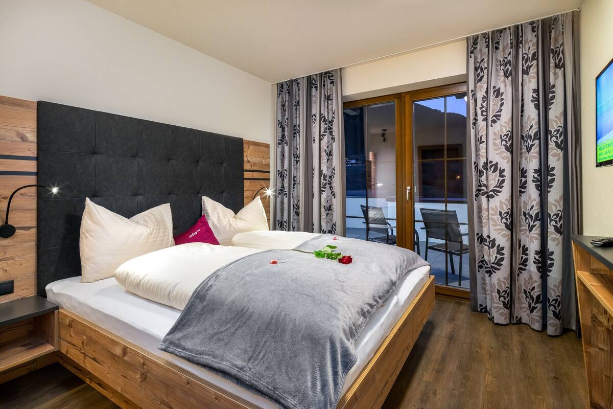 A modern bedroom with a large bed, wooden headboard, and a view of the outdoors through a sliding glass door.