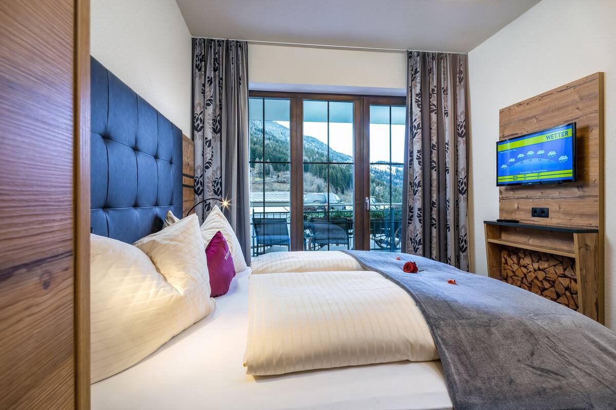 A hotel room with a large bed, a television mounted on the wall, and a view of a mountainous landscape through the window.