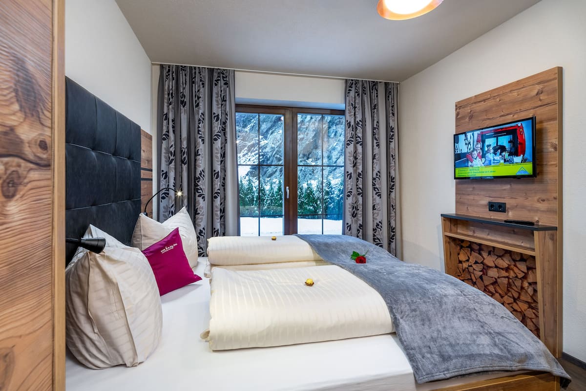 A modern bedroom with a large bed, a TV mounted on a wooden wall, and a window with curtains.