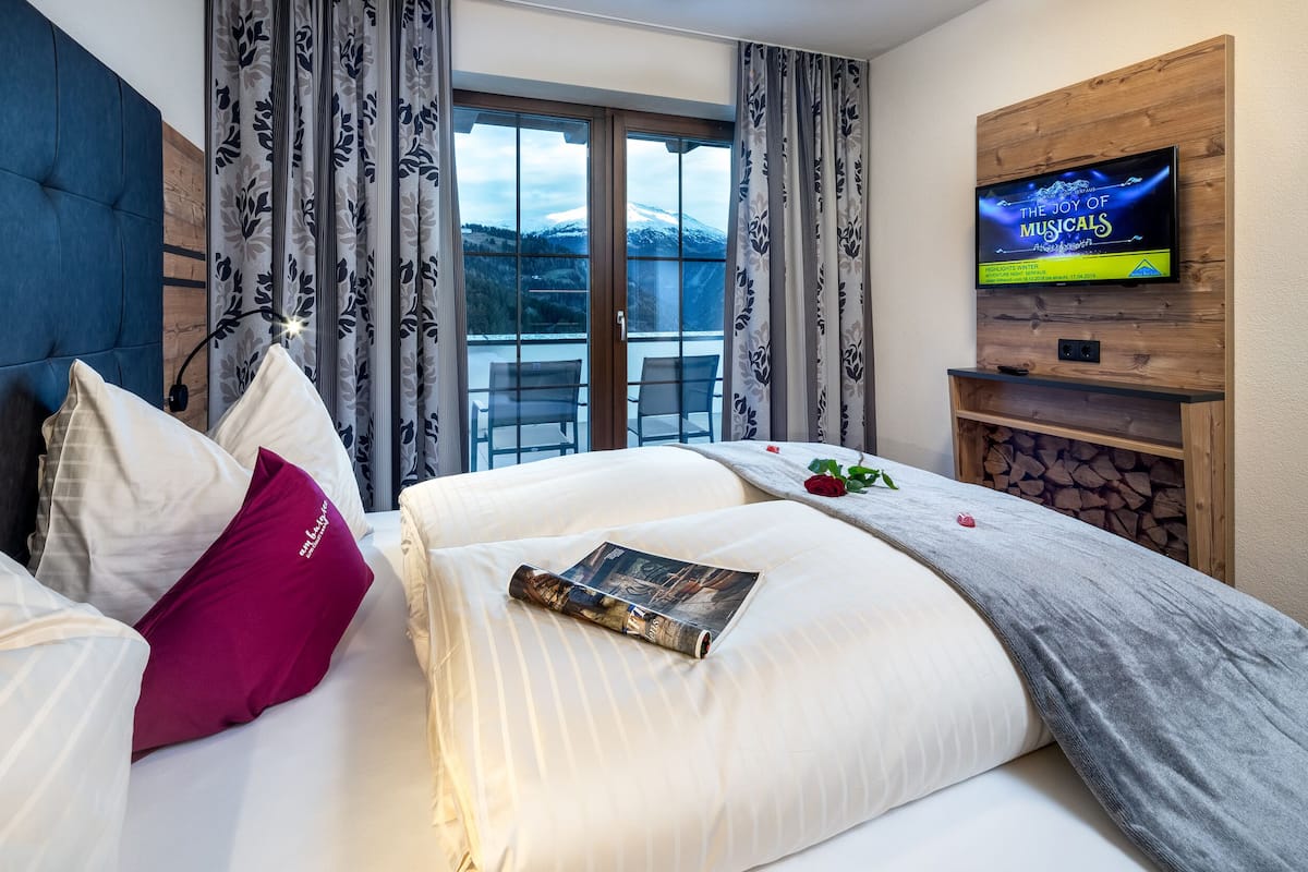 A hotel room with a bed, a mounted TV, a view of mountains, and a fireplace.