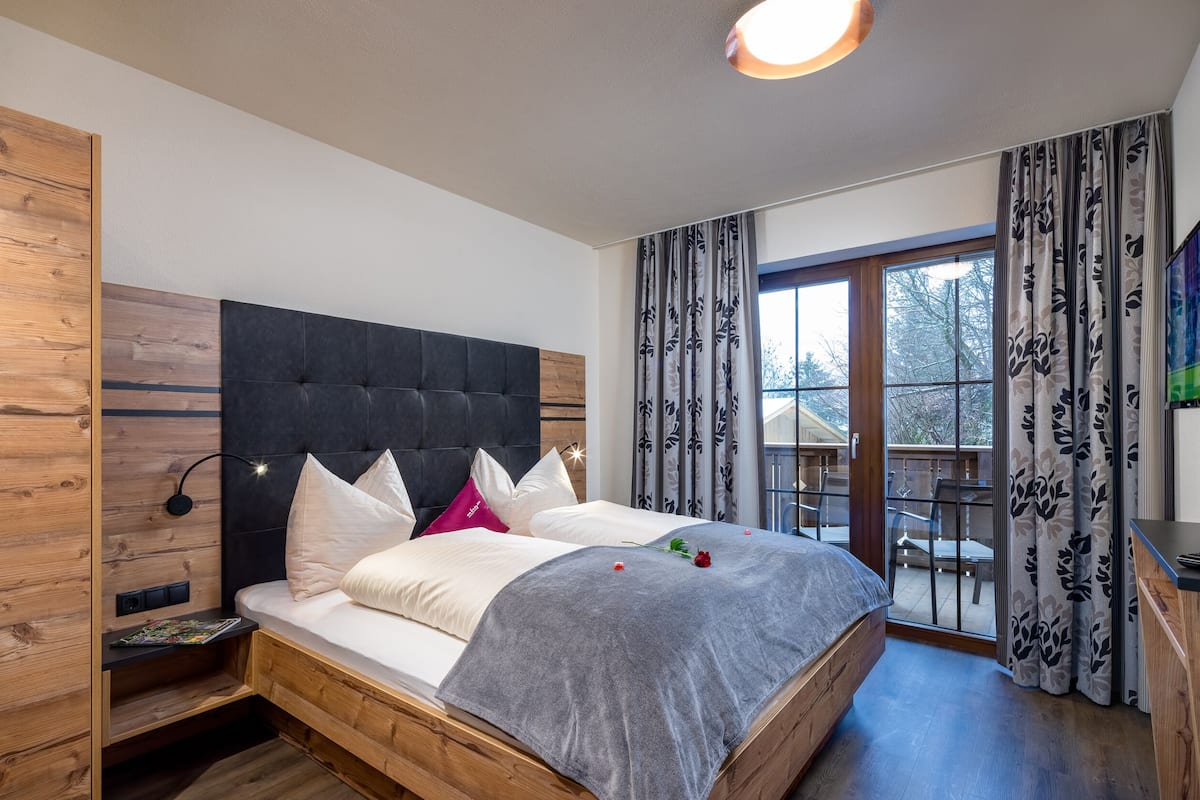A bedroom with a large bed, wooden headboard, and a balcony with a view.
