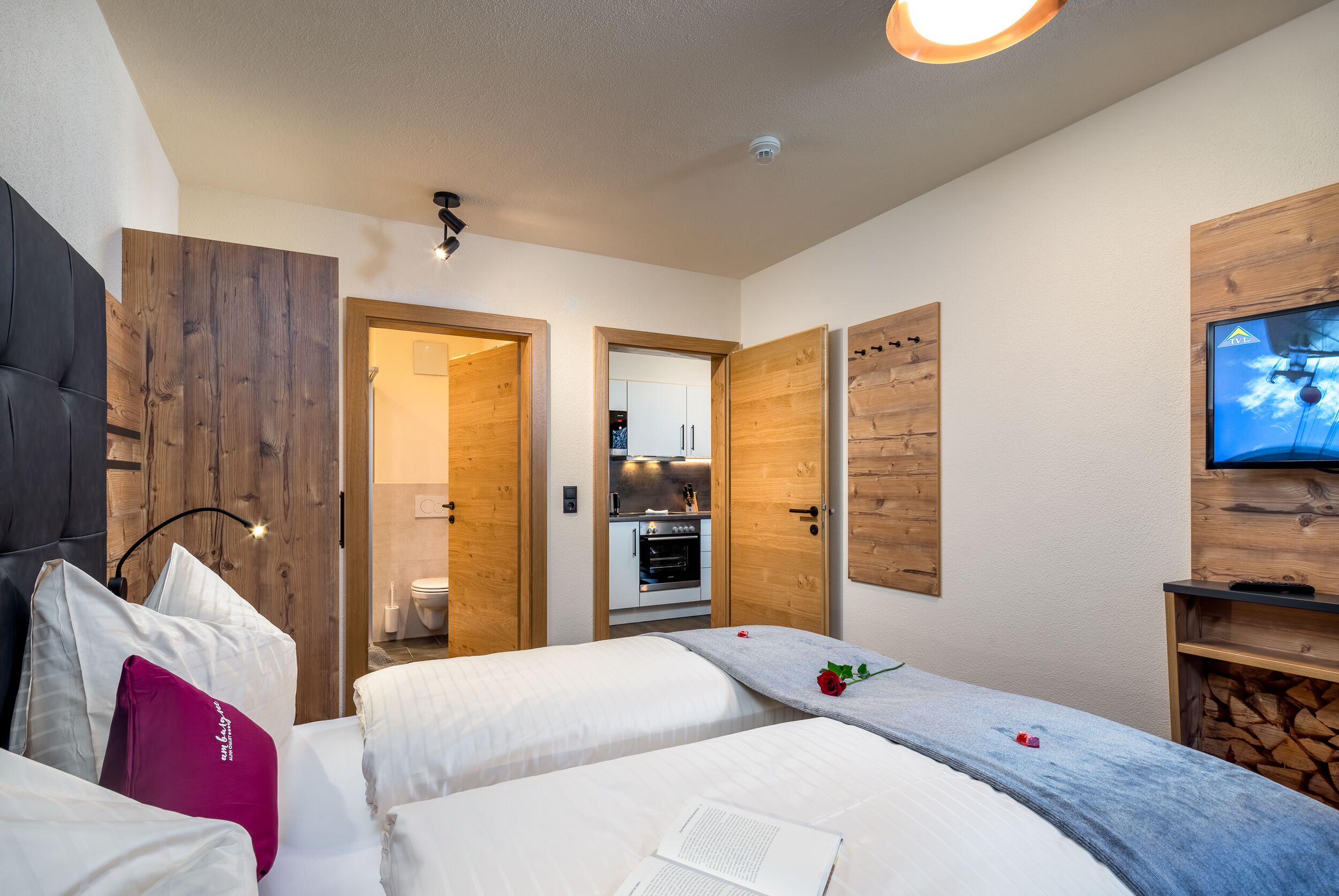Ein modernes Hotelzimmer mit einer Wandpaneinung aus Holz, einem Fernseher und einer Küchenzeile im Hintergrund.