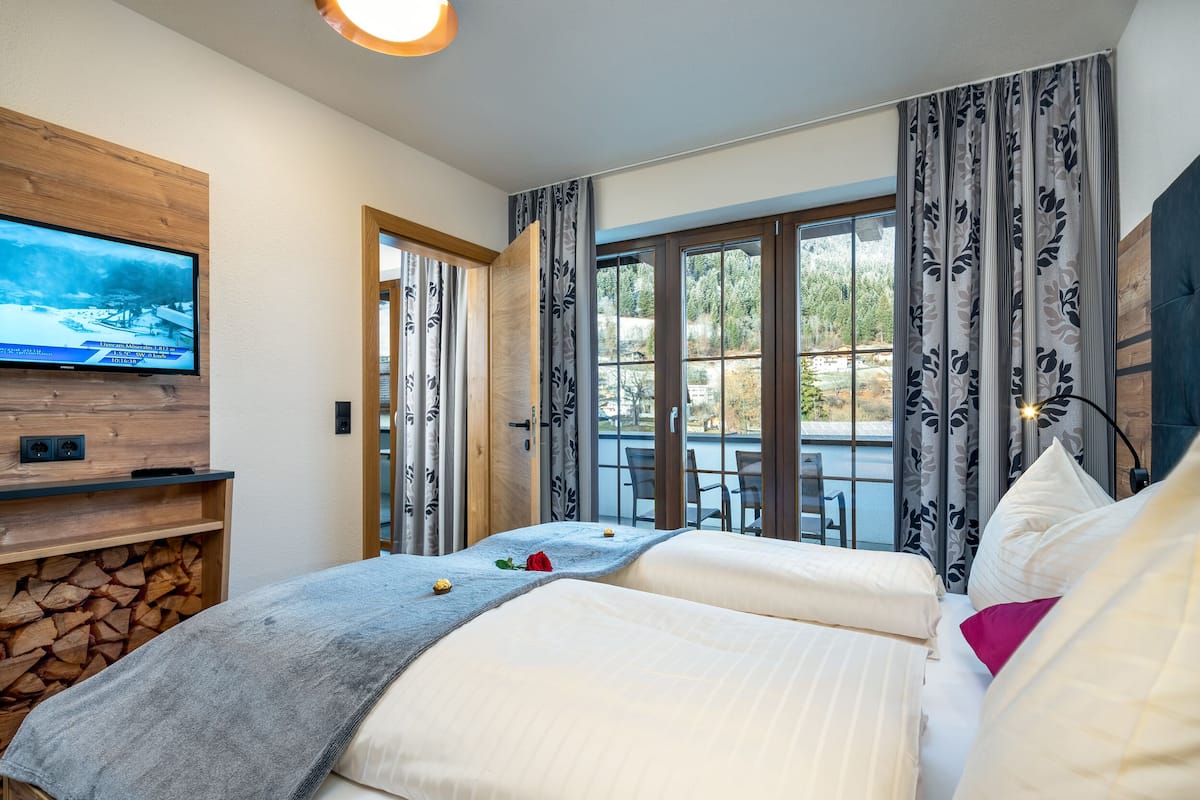 A hotel room with a bed, a TV mounted on a wooden panel, a fireplace, and a view of the outdoors through large windows.