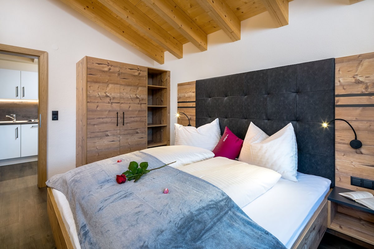 A bedroom with a large bed, wooden wardrobe, and a modern headboard.