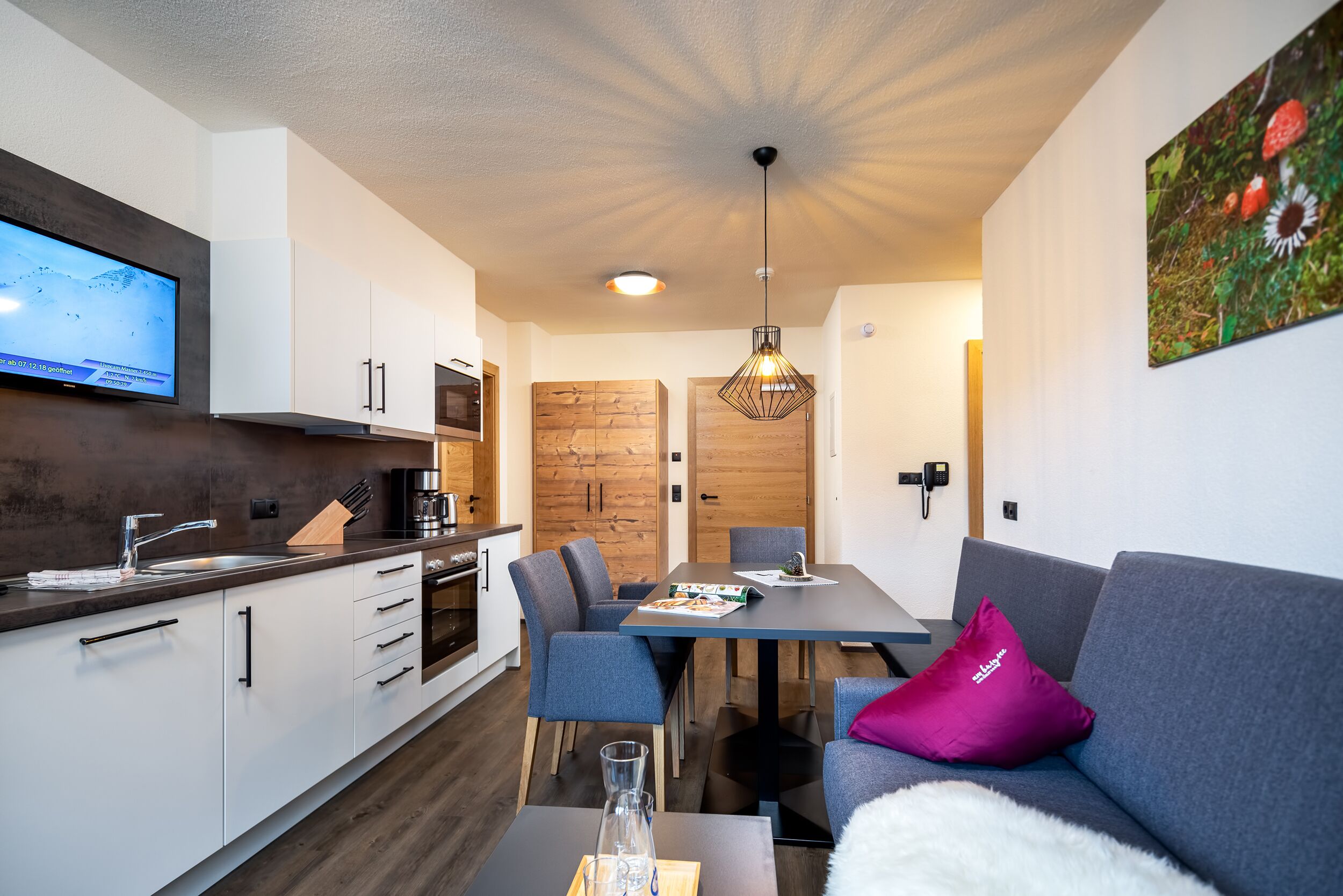 A modern kitchen with a flat-screen TV, wooden cabinets, and a dining area with a table and chairs.