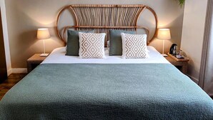 A hotel room with a bed, two bedside lamps, a hanging plant, and a textured bedspread.