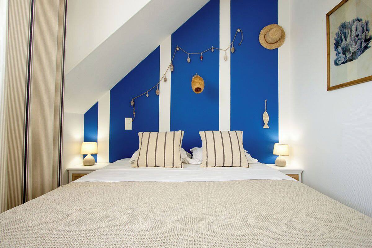 A bedroom with a large bed, two bedside tables with lamps, a blue accent wall, and a framed artwork on the wall.