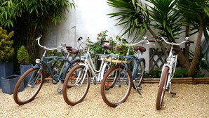 Three bicycles parked on a gravel surface with a concrete wall and greenery in the background.