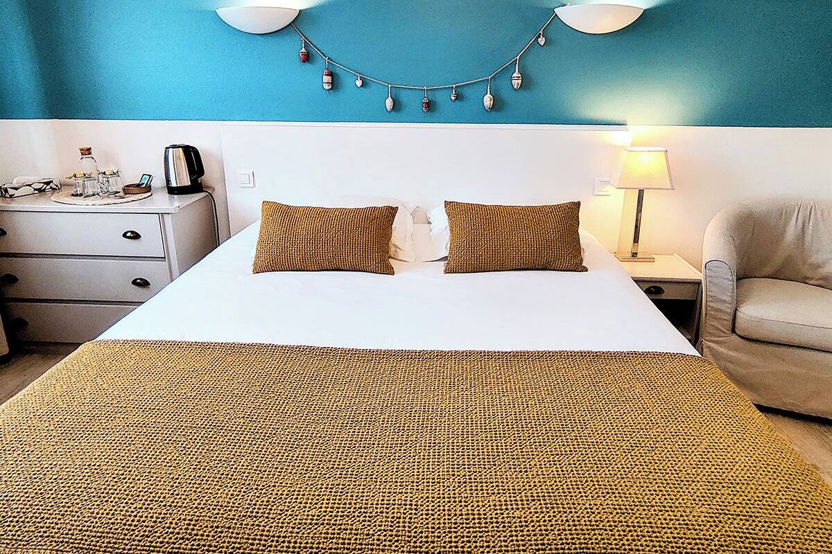 A hotel room with a bed, a nightstand, a lamp, a chair, and a wall-mounted string of decorative items.