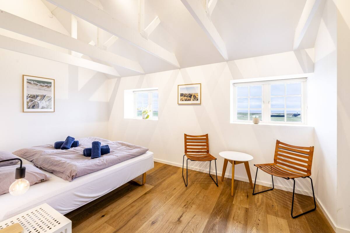 Un dormitorio con cama, dos sillas, una mesita y ventana con vistas.