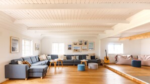 Un salon spacieux doté d’un plancher en bois, d’un canapé d’angle gris, d’un pouf bleu et d’une poutre en bois au plafond.