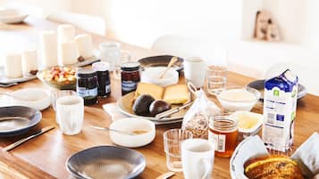 A breakfast table with various food items, including bread, cheese, and fruits, along with several cups and a jug of juice.