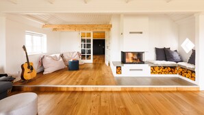 Un salon spacieux avec un plancher en bois, une cheminée, un canapé et une guitare.