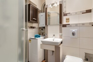 A compact bathroom with a white sink, a towel dispenser, a mirror, and a built-in heater. - Elite Apartments City Center Korzenna (Gdansk)