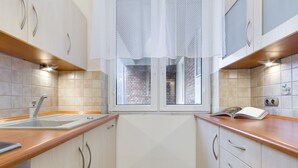 Ett modernt kök med vita skåp, en bänkskiva i trä, ett fönster med utsikt över en byggnad med tegelväggar och en bok som ligger på bänkskivan.