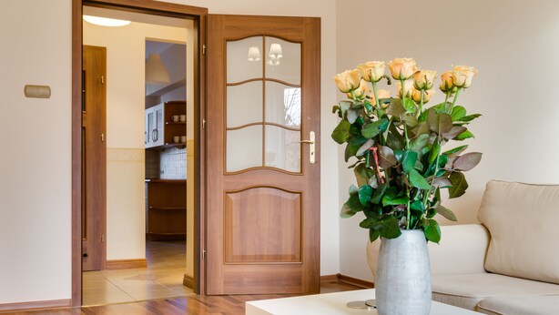 Ett rum med en dörr av trä, ett vitt bord med en vas med blommor och en beige soffa.