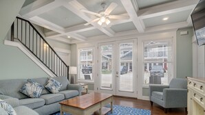 Un salon spacieux avec un escalier, un ventilateur de plafond et une grande fenêtre équipée de stores.