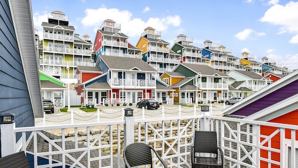 Une rangée de maisons de plage aux couleurs vives, dotées d’une terrasse en bois et de chaises en osier.