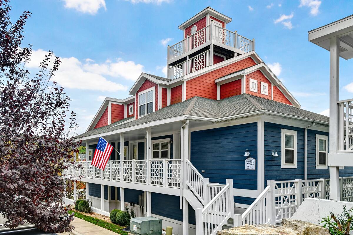 A two-story house with a balcony, a flag, and a sign indicating the house number.