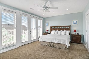 A bedroom with a large bed, a ceiling fan, and a view through the sliding glass doors.