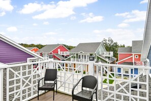 A balcony with white railings, two wicker chairs, and colorful buildings in the background.