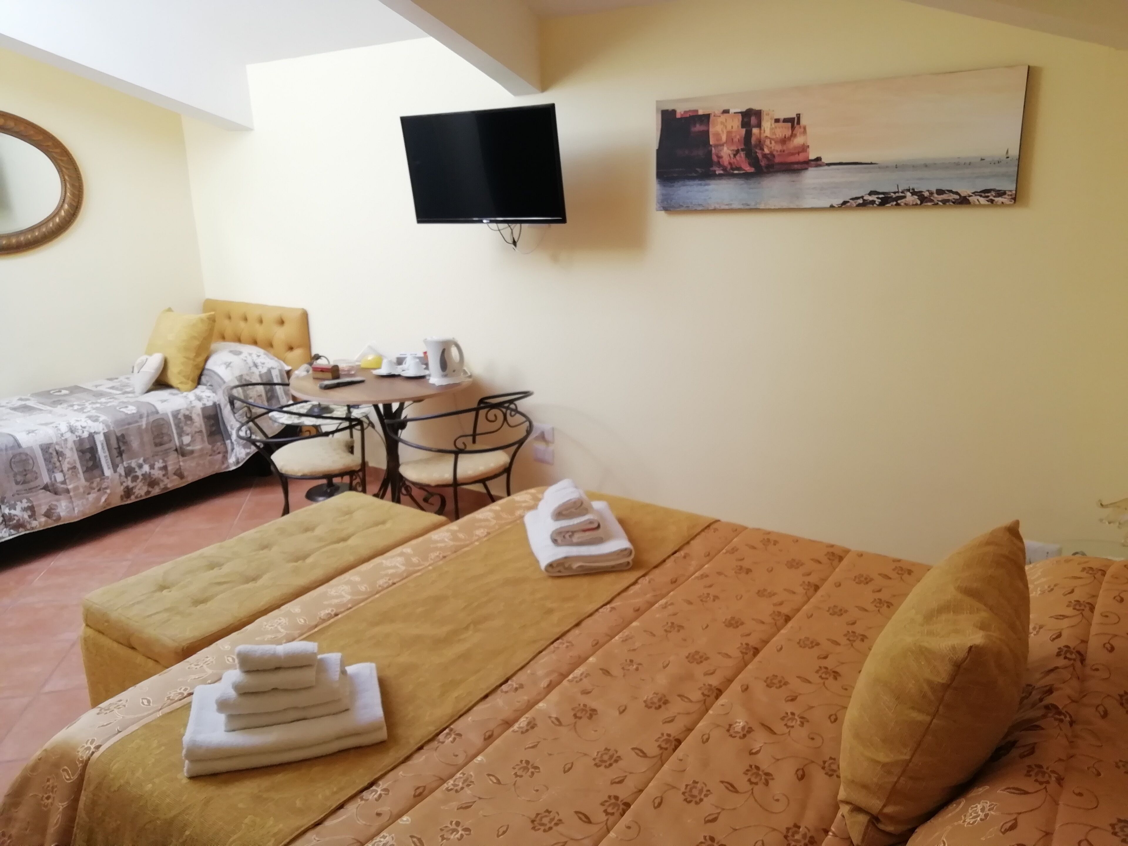A hotel room with a bed, a small table with chairs, a television, and a painting on the wall.