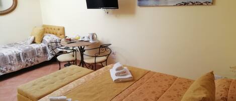 A hotel room with a bed, a small table with chairs, a television, and a painting on the wall.