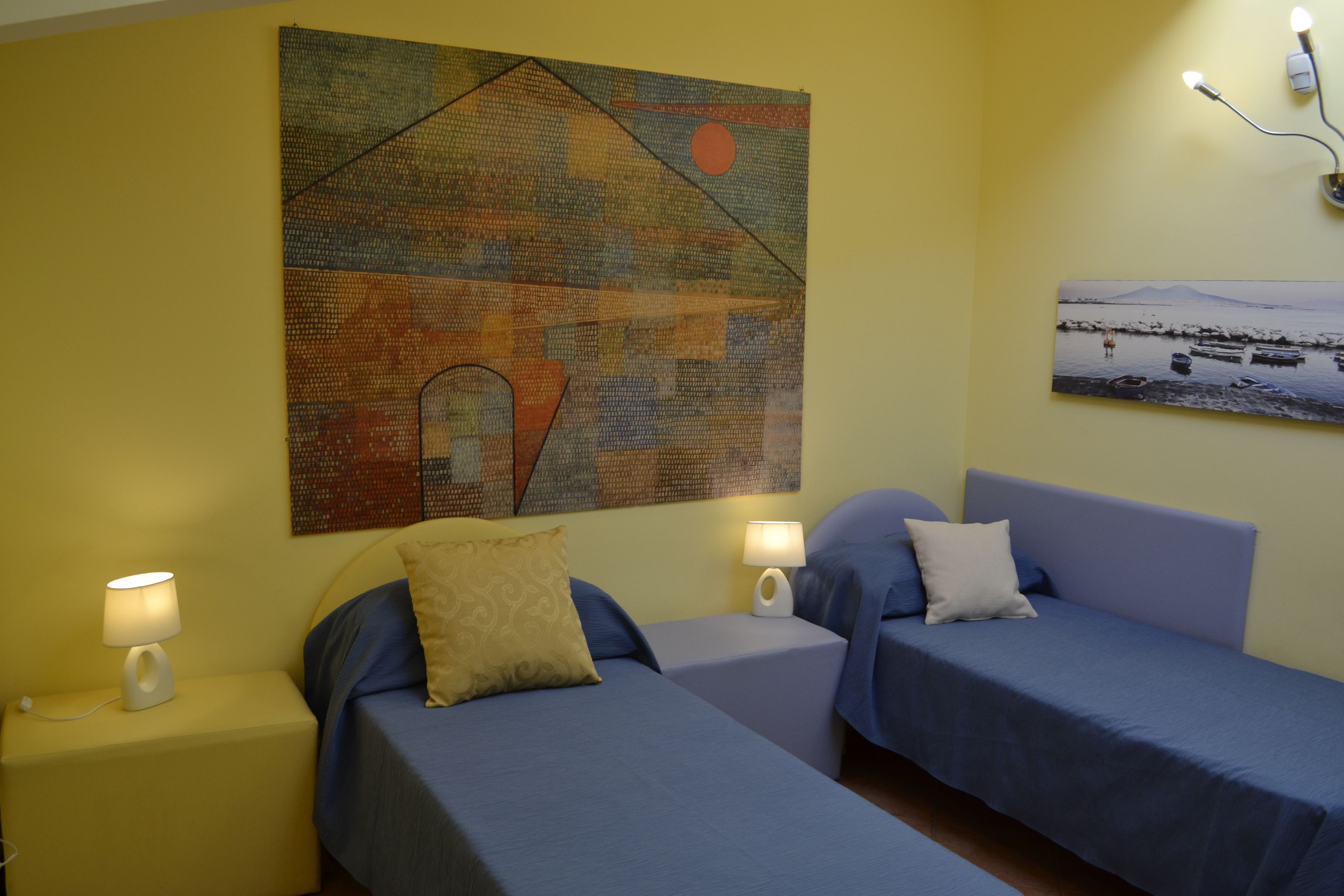 A hotel room with two beds, a yellow wall, and artwork.