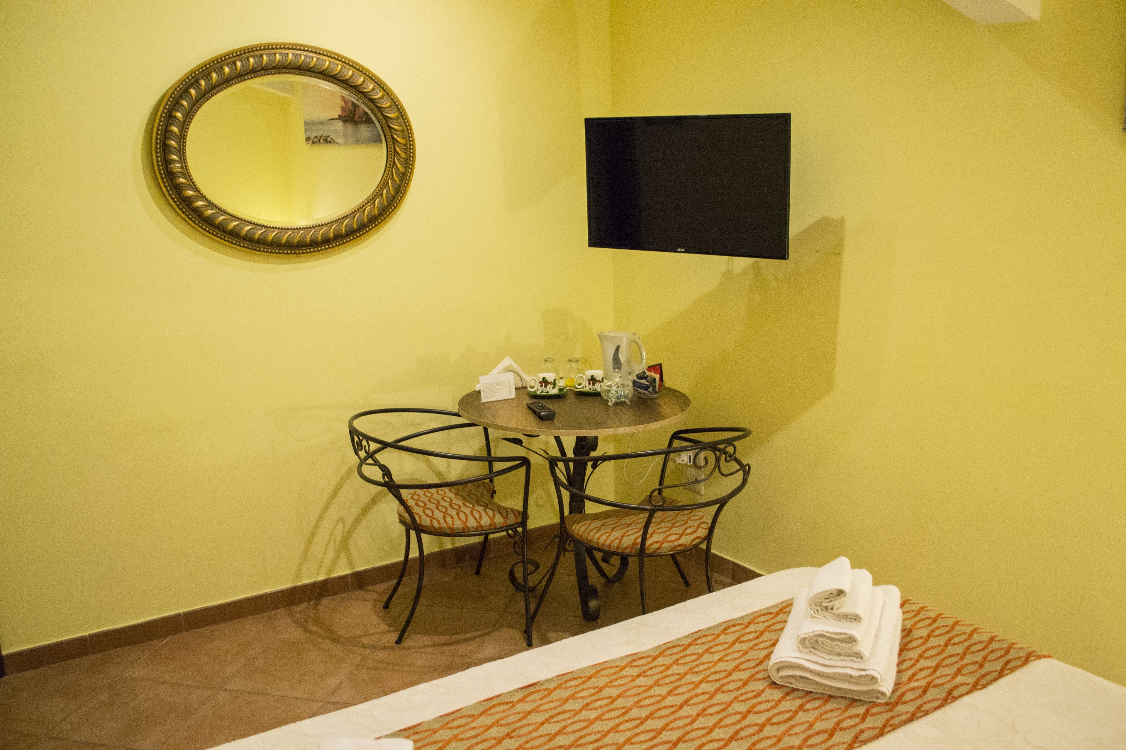 A hotel room with a bed, a round table with chairs, a television, and a mirror on the wall.