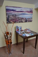 Een kamer met een tafel waarop reisbrochures liggen, een stadsgezicht in een lijst en een decoratieve vaas met takken.