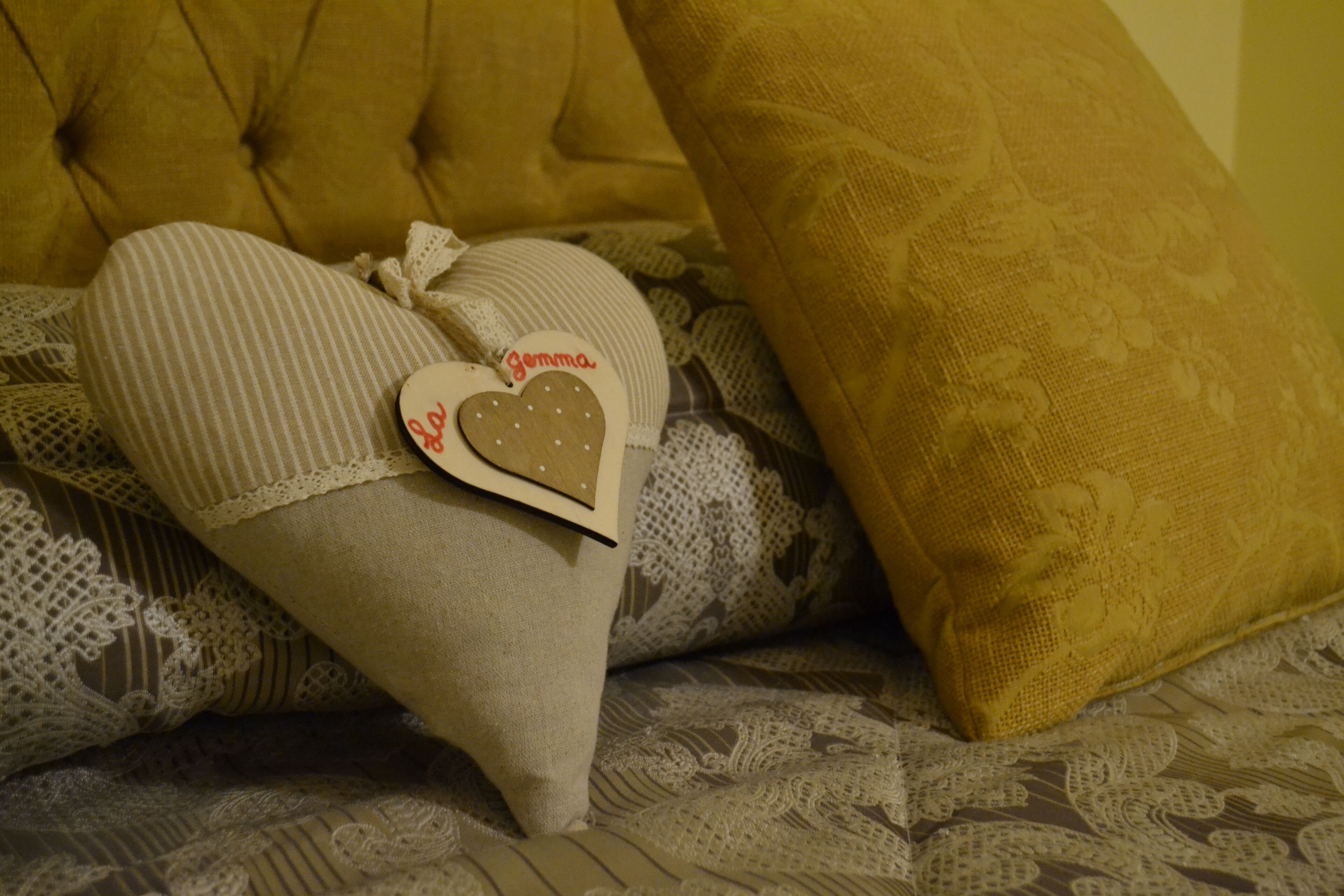 A bed with a tufted headboard, a striped pillow, and a heart-shaped pillow with a tag.