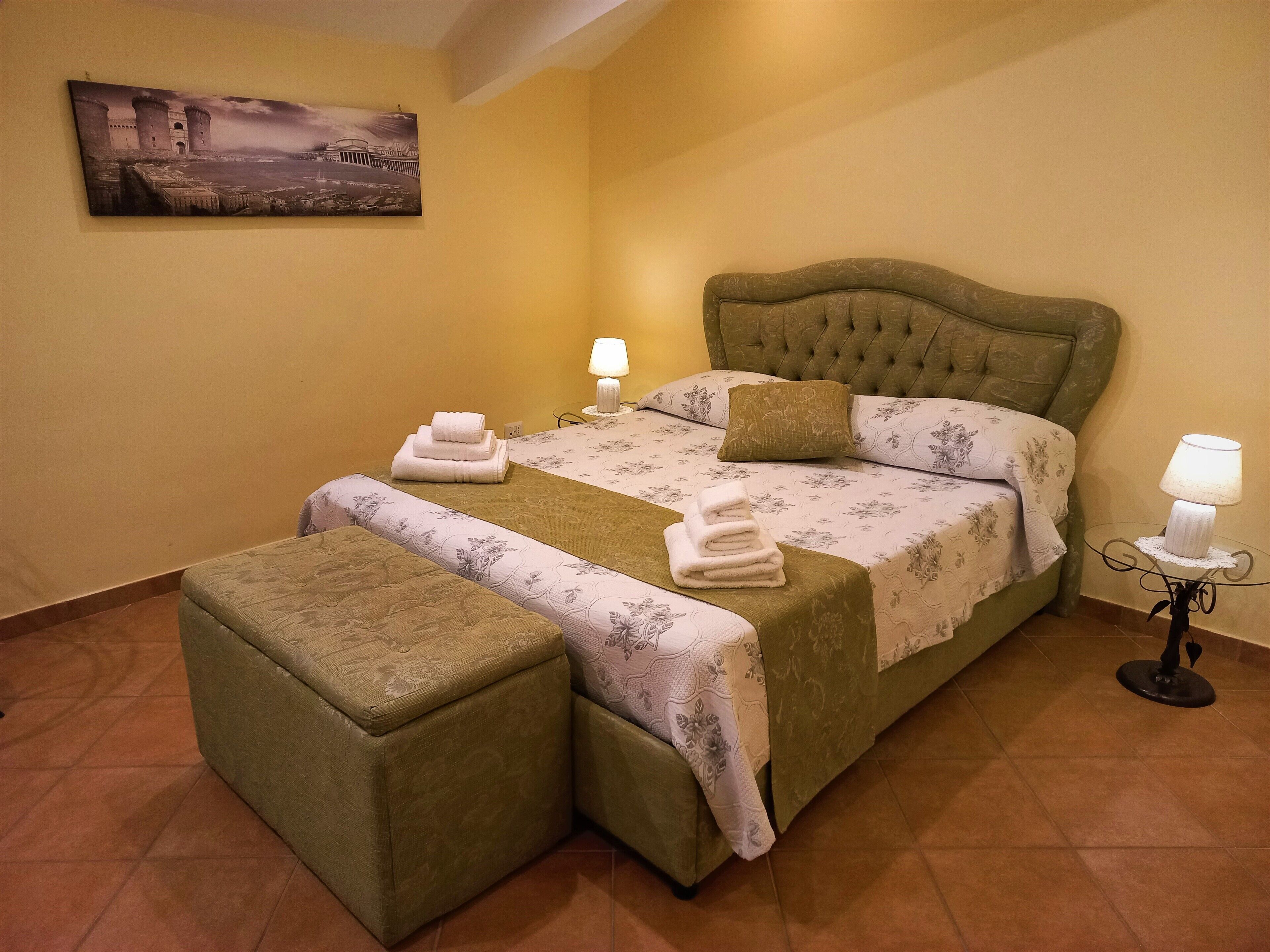 A neatly made bed with floral bedding, two bedside lamps, and a folded towel on the bed.