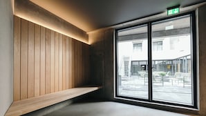 A corner of a room with a wooden bench, a large window, and a visible exit sign. - Exeter Hotel (Reykjavik)