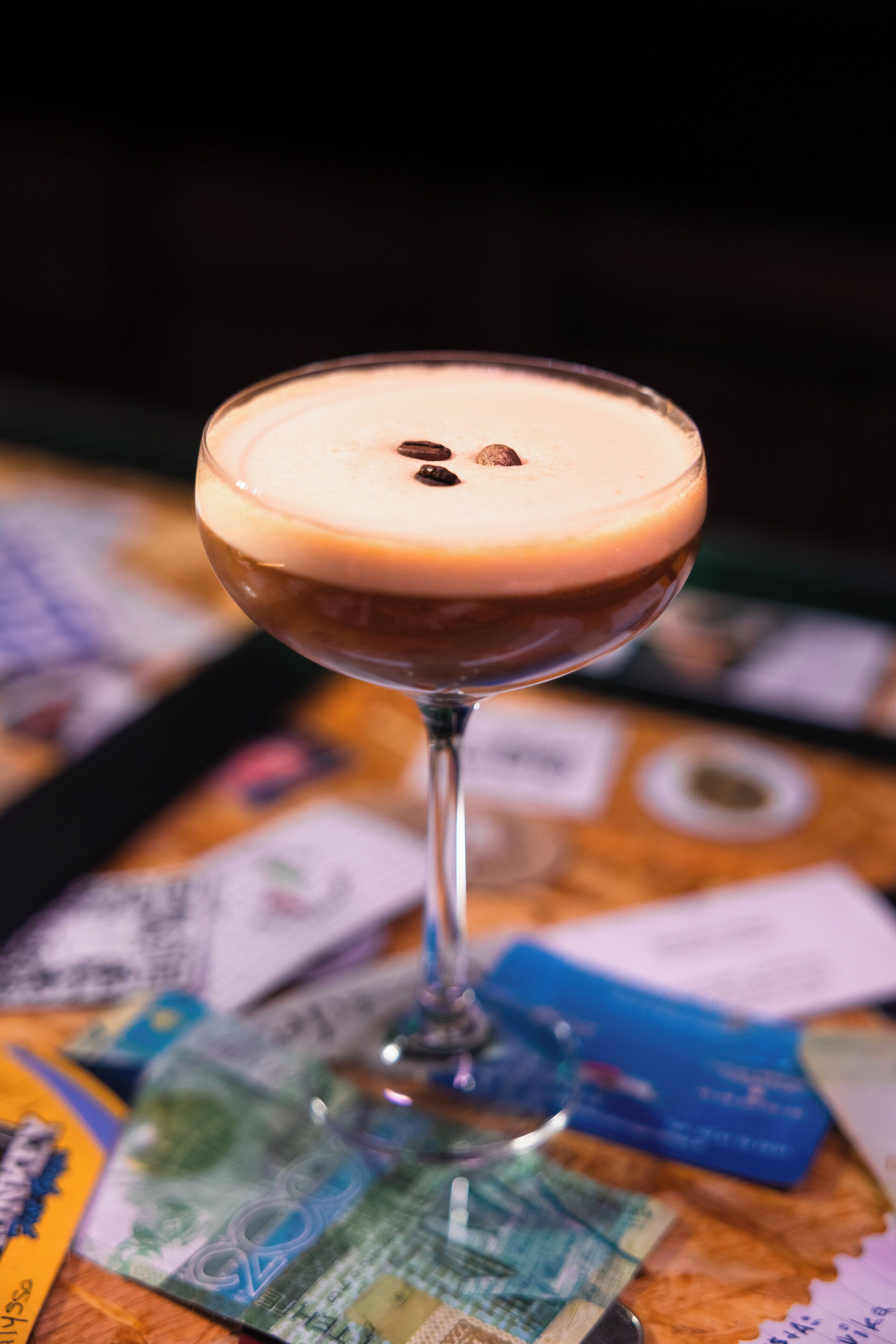 Un cóctel en una copa de martini con una espuma arriba, sobre una mesa con varias tarjetas y billetes.